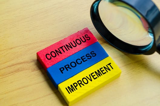Continuous process improvement text on multicolored wooden blocks with magnifying glass background. Continuous improvement concept.