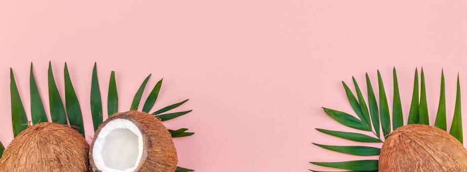 Creative flat lay top view of green tropical palm leaves coconut fruits and coconut oil cosmetics for skin and hair care on pink paper background copy space. Minimal tropical summer beauty spa concept