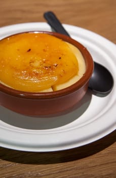 Catalan cream served in a clay bowl with a black spoon on a wooden background. Selective focus