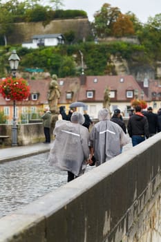Tourists with rain wear walking across the old Main bridge, alte Mainbrucke in Würzburg in Germany in the rain