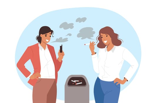 Smoking women use tobacco cigarettes or vape device, standing near garbage can. Two positive smoking girls discussing new alternative to nicotine, which causes cancer and lung disease