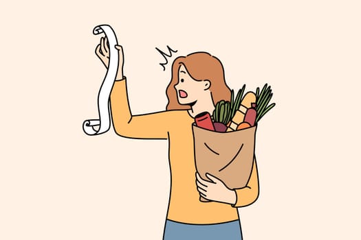 Huge bill for healthy food shocks woman who opens mouth, reading store receipt. Girl with bag healthy food products, disoriented due to sharp inflation of costs for organic fruits and vegetables.