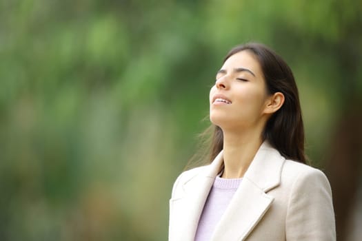 Happy woman breathing fresh air in winter standing in a park