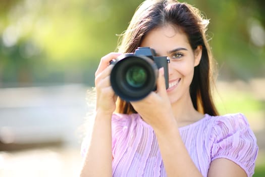 Happy photographer taking picture of you with mirrorless camera in a park