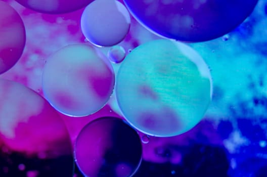 Macro shot of oil droplets forming clusters with multicolored blue gradient.