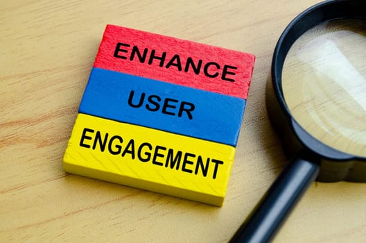 Top view of Enhance User Engagement text on multicolored wooden blocks with magnifying glass background.