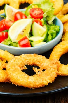 Delicious Fried squid rings and fresh vegetable salad. Close up.