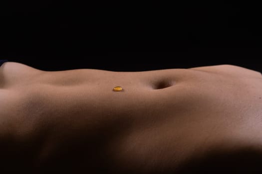Beautiful seductive young female makes honey on a black background. Drops of honey on her belly.