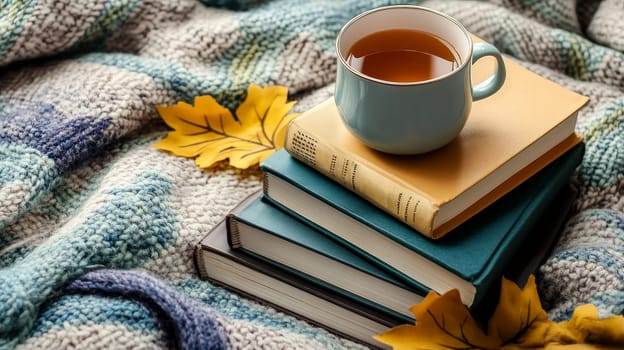 Stack of books, tea cup, and autumn leaves on knitted blanket. Hygge lifestyle concept for fall season relaxation and literature enjoyment.