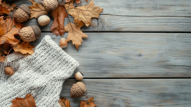 Warm knitted scarf with fall leaves, acorns, and pine cones on weathered wooden background, creating a cozy autumn atmosphere with copy space.