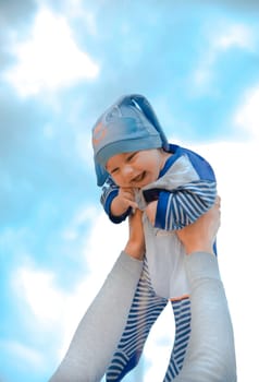 A joyful, happy baby is gently lifted high into the air against a stunningly beautiful blue sky above