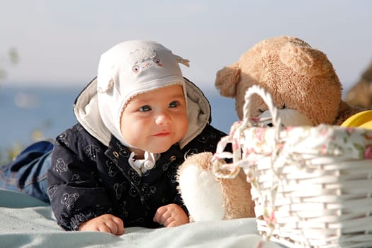 A cute kid on a picnic lies next to a teddy bear in a serene and beautiful outdoor environment by the sea