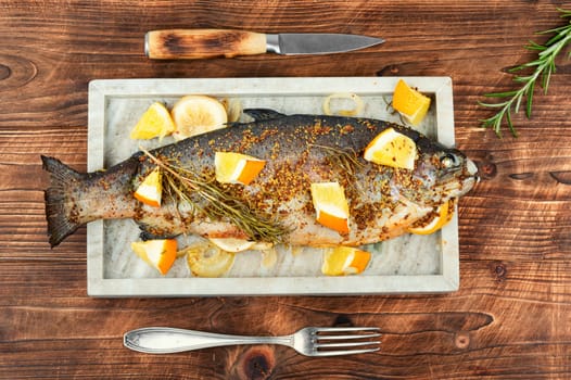 Trout fried with orange and rosemary on wooden background.