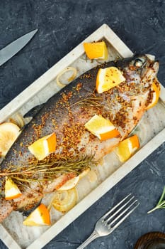 Trout fried with orange and rosemary on wooden background.