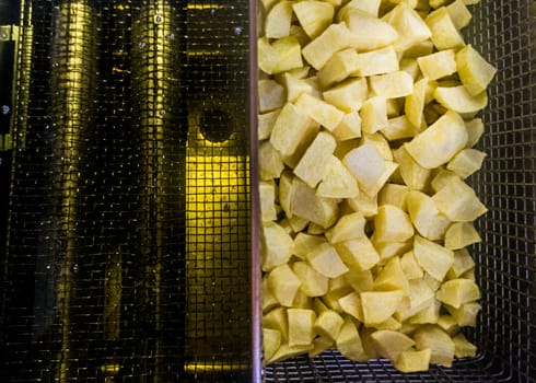 Basket of dices potatoes in the deep fryer of a restaurant kitchen. Overhead view