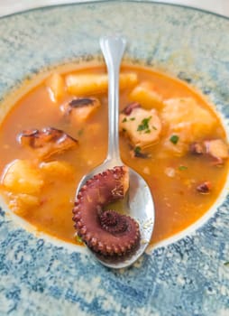 Potato stew with seafood displayed over table. Octopus tentacle on spoon in close-up