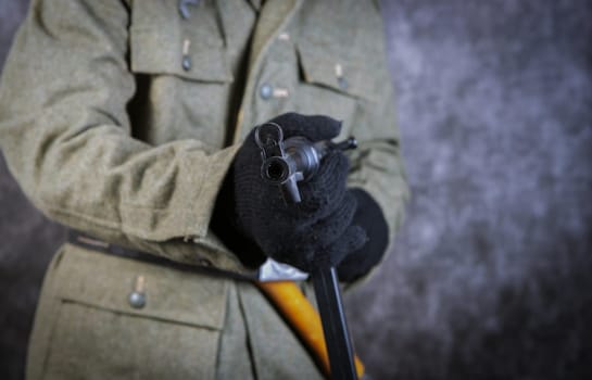 A german man in a military uniform holding a gun. The man is wearing a black glove and a green jacket