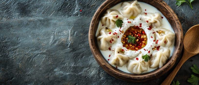 Traditional Georgian khinkali dumplings served in a creamy yogurt sauce with red chili oil and herbs in a rustic wooden bowl.