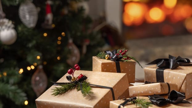 Wrapped Christmas gifts with black ribbon bows against burning fireplace and christmas tree decorated with lights. Warm winter family atmosphere, Magical Holiday time