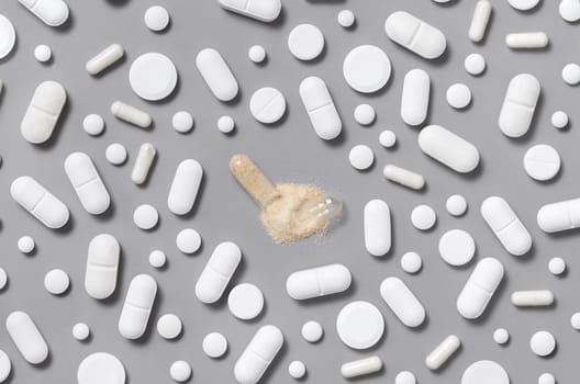 Mix of white medical capsules and pills with opened beige capsule in the middle on grey top view. Medicinal treatment. Taking dietary supplements. Assorted pharmaceutical products