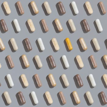 Patern of beige and brown medical capsules with one yellow on grey top view, hard shadows. Preventive medicine and healthcare, herbal dietary supplements and vitamins