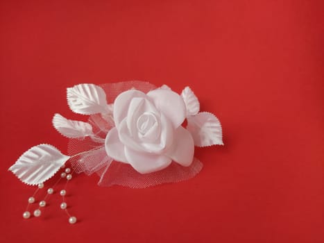 A stunning white rose stands out beautifully against a rich red background, complemented by soft leaves and small pearl accents, ideal for a wedding setting.