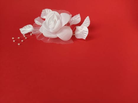 A stunning white rose stands out beautifully against a rich red background, complemented by soft leaves and small pearl accents, ideal for a wedding setting.