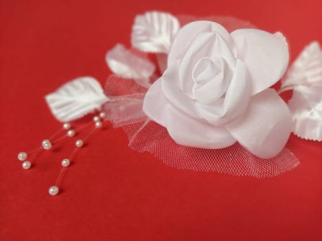 A stunning white rose stands out beautifully against a rich red background, complemented by soft leaves and small pearl accents, ideal for a wedding setting.