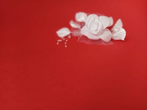 A stunning white rose stands out beautifully against a rich red background, complemented by soft leaves and small pearl accents, ideal for a wedding setting.
