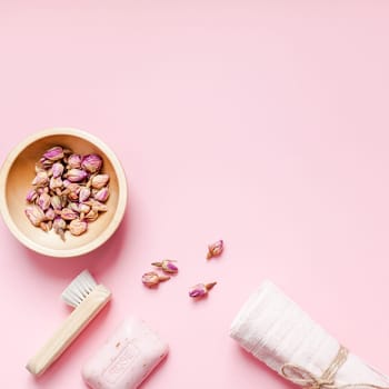 Spa, beauty cosmetics and body care treatment concept with copy space. Creative top view flat lay composition with bath accessories, organic DIY rose soap and dry flowers in a bowl on pink background