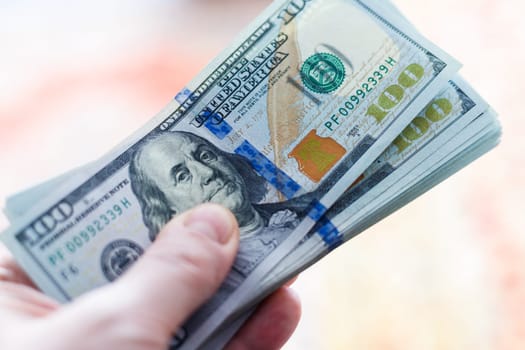 left Caucasian male hand holding stack of us dollar banknotes, closeup with blurry background