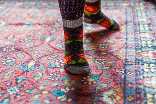 legs in warm woven wool socks standing on red ornate carpet floor at home backlit with a window light