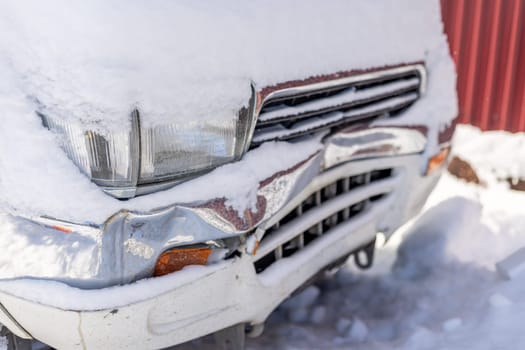 snow covered white SUV car with damaged front bumper at sunny winter day