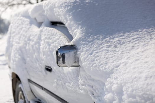 chrome coated side mirror of snow covered white SUV at sunny winter day