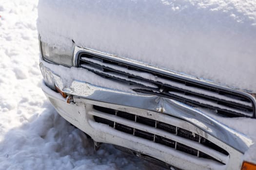 snow covered white SUV car with damaged front bumper at sunny winter day