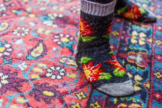 legs in warm woven wool socks standing on red ornate carpet floor at home backlit with a window light