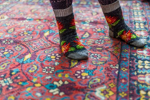 legs in warm woven wool socks standing on red ornate carpet floor at home backlit with a window light