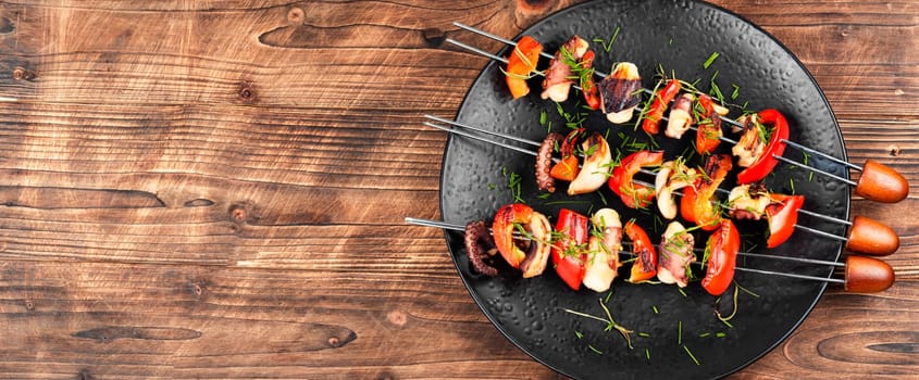 Grilled octopus skewers garnished with bell pepper. Seafood on a black plate.
