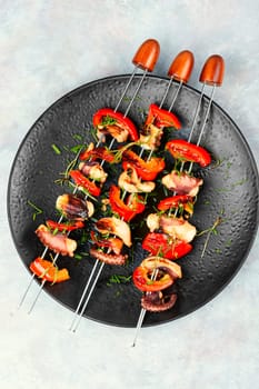 Grilled octopus skewers garnished with bell pepper. Seafood on a black plate.