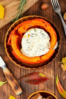 Autumn pumpkin baked with camembert cheese on a rustic wooden table. Healthy food.