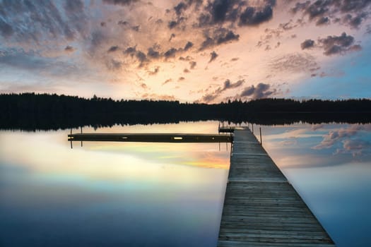 Wooden jetty at sunset on a Swedish lake. The colors of the sunset are reflected in the water. A bathing lake in the Scandinavian countryside