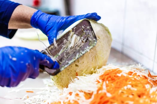 hands in blue gloves cutting cabbage with special double blade slit cabbage shredder knife during sauerkraut preparation