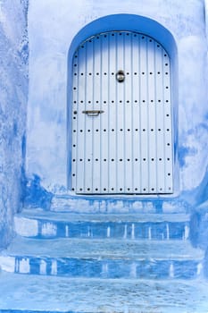 Blue stairs leading to an azure blue door in the city of Chefchaouen closeup.  Morocco. Vertically.