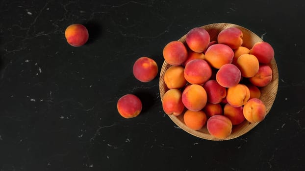 Apricots in small wooden bowl, some of them scattered on black marble like board, view from above