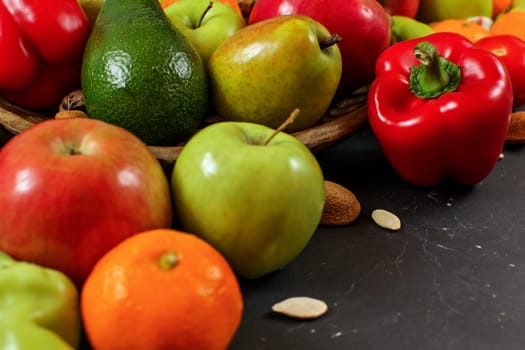 Mixed fruits and vegetables - red peppers, avocado, apples, pears, tangerines, pecan nuts, almonds and pumpkin seeds on black marble like board