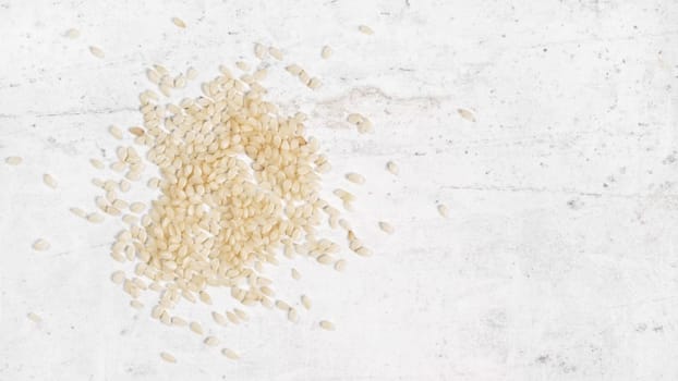 White sesame - Sesamum indicum - seeds on white stone like board, view from above, space for text right side