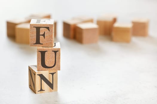 Three wooden cubes with word FUN, on white table, more in background, space for text in right down corner