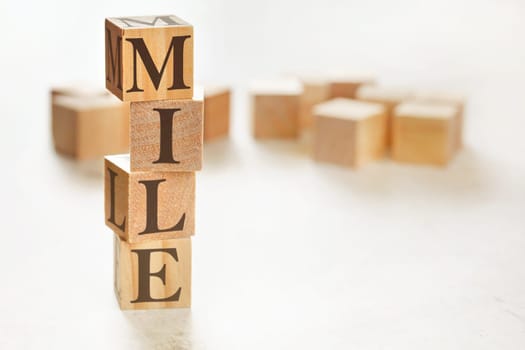 Four wooden cubes arranged in stack with word MILE (meaning Maximum Impact Little Effort) on them, space for text / image at down right corner