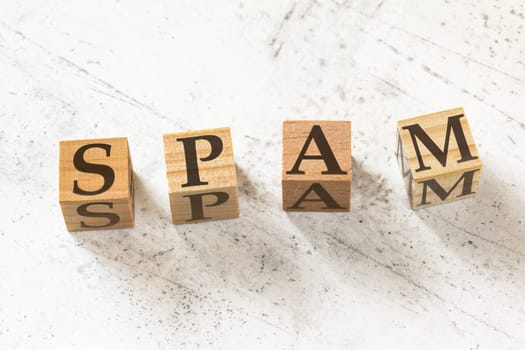 Four wooden cubes with word SPAM on white working board.