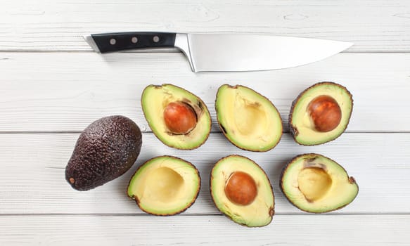 Avocado - Hass / Bilse variety - halves arranged on white boards desk, some of them over ripen, chefs knife above, overhead photo